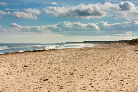 Sunny beach with blue sky, clouds and breaking waves on Northumberland coast, North East England.の写真素材