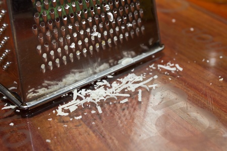 Slivers of grated parmesan cheese next to worn cheese grater.の写真素材