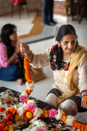 Delhi / India - October 2, 2019: Hindu women weaving flower garlands, decorative wreath of flowers,...