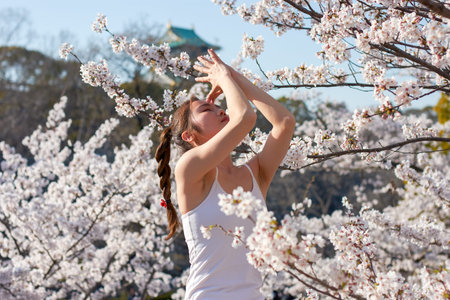 Osaka / Japan - March 28th 2018: Girl practicing yoga in Osaka castle park during the sakura cherry...