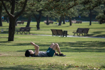Tokyo / Japan - April 22, 2018: Man resting on the grass lawn inside Kokyogaien Park next to the Imperial Palace in Tokyo, Japanのeditorial素材
