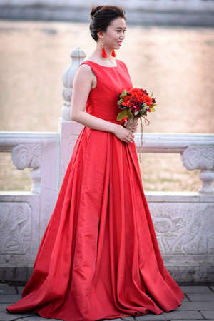 Beijing / China - April 9, 2016: Pretty Chinese bride in red dress posing outdoors in Houhai lake park in Beijing, Chinaのeditorial素材