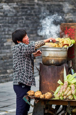 Qufu / China - October 13, 2018: Woman cooking corn clips on a street food stall in Qufu, birthplace of philosopher Confucius, Shandong province, Chinaのeditorial素材
