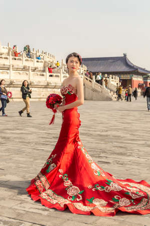 Beijing / China - April 5, 2015: Pretty Chinese girl in red wedding dress, posing in front of the Temple of Heaven in Beijing, Chinaのeditorial素材