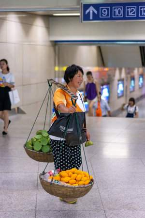 Nanjing / China - July 30, 2015: Woman with a wooden carrying pole selling fruits and water in Nanjing subway, Nanjing, Chinaのeditorial素材