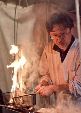 Wakayama / Japan - March 29th 2018: Man grilling meat, evening street food stall at Wakayama city festival in Wakayama, Japanのeditorial素材