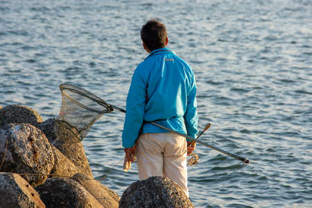 Japanese man with a fishing net rod fishing at seashore in Osaka Bay, Japanの写真素材