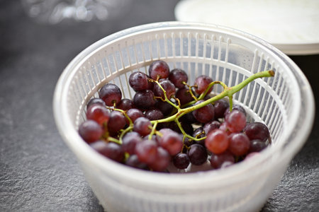 Fresh red grapes in a white plastic colander on a dark kitchen surface.の写真素材