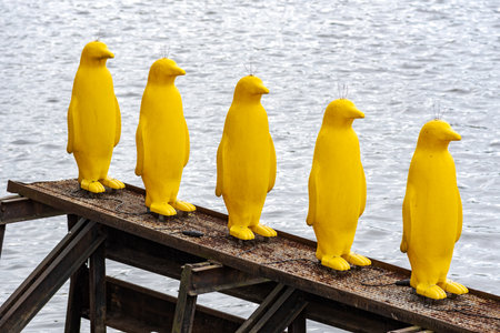 Five yellow penguin sculptures on a metal platform by the water.の写真素材