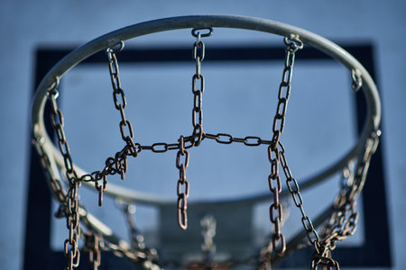 Close-up of a basketball hoop with a chain net against a blue sky.の写真素材