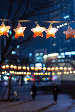 Star-shaped lights hanging in a cityscape at night, with blurred pedestrians and buildings in the backgroundの写真素材