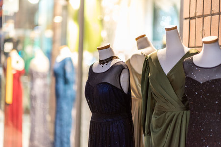 A display of elegant evening gowns on mannequins in a boutique, showcasing various styles and colors, with a blurred background of more dressesの写真素材