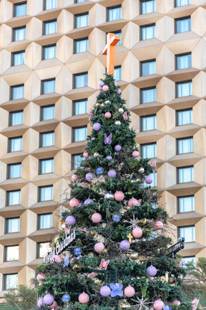 A decorated Christmas tree with pink and purple ornaments and butterflies in front of a modern building.の写真素材