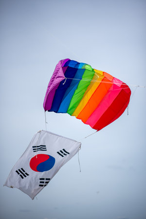 A colorful rainbow kite flying alongside the South Korean flag against a clear skyの写真素材