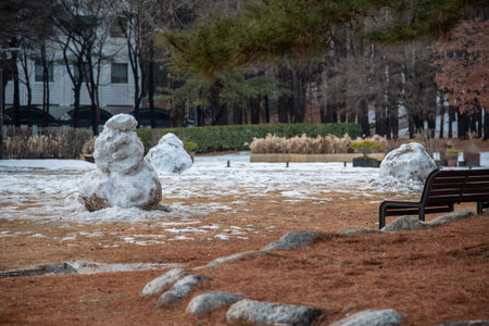 A snowy park with melting snowmen and bare trees in winter.の写真素材