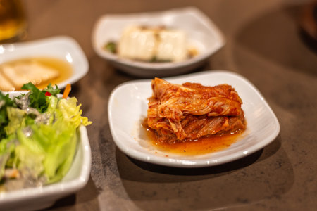 A plate of kimchi served with side dishes including tofu and salad, Korean food in a restaurantの写真素材