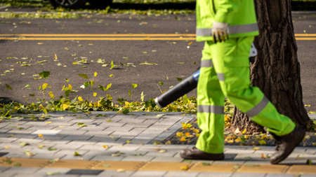 Worker in high-visibility gear using a leaf blower on a sidewalk in Seoul, South Korea on 18 November 2023の写真素材