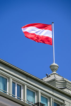 Austrian flag waving on a building rooftop against a clear blue skyの写真素材