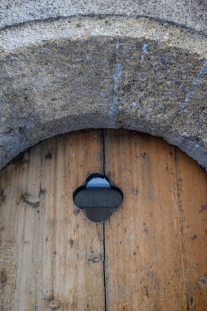 Rustic wooden door with small clover-shaped window in stone archway.の写真素材