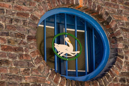 A circular window with blue bars and a decorative swan emblem on a brick wallの写真素材