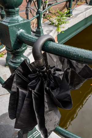 A black umbrella hangs on a green railing by a canal.の写真素材