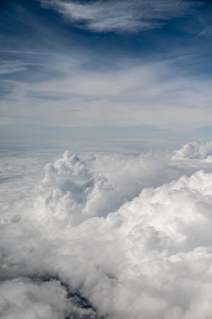 Aerial view from an airplane of fluffy white clouds under a blue sky with wispy cloudsの写真素材