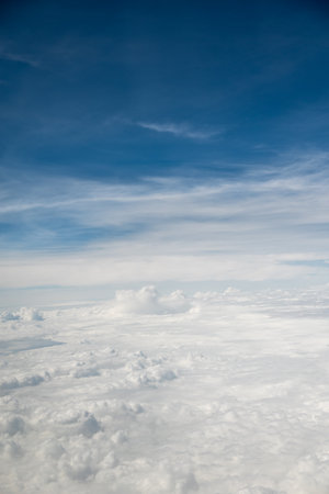 Aerial view from an airplane of fluffy white clouds under a blue sky with wispy cloudsの写真素材
