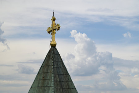 A church steeple with a golden cross against a cloudy skyの写真素材