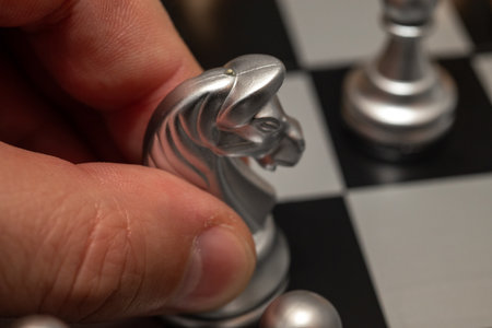 Hand moves white knight on chessboard with close up chess game piecesの写真素材