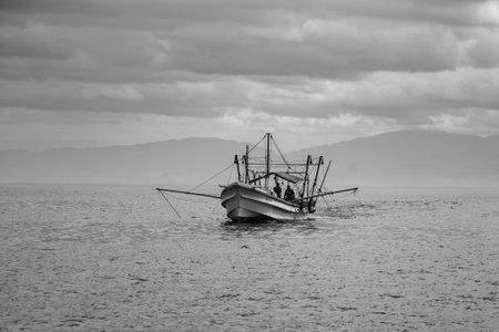 A lone fishing boat on a calm sea under a cloudy skyの写真素材