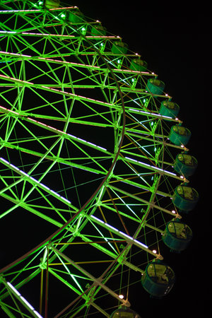 Illuminated green Ferris wheel against a dark night skyの写真素材