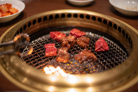 Close-up of meat grilling on a Korean style barbecue grill with tongsの写真素材