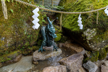 A dragon statue fountain in a Japanese garden with moss-covered rocks and traditional paper decorationsの写真素材