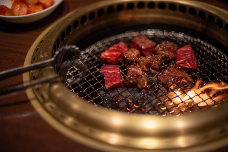 Close-up of meat grilling on a Korean style barbecue grill with tongsの写真素材