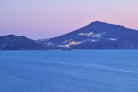 Twilight view of a serene coastal landscape with distant hills and illuminated buildings.の写真素材