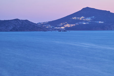 Twilight view of a serene coastal landscape with distant hills and illuminated buildings.の写真素材
