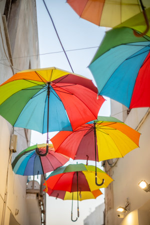 Colorful umbrellas hanging in a narrow alleyway between white buildings in Mediterranean town in Greeceの写真素材