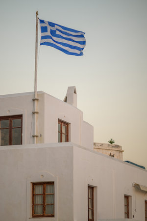 Greek flag waving on a white building at sunsetの写真素材