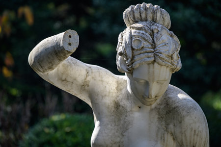 Weathered marble classical statue of a woman with a broken arm in a garden.の写真素材