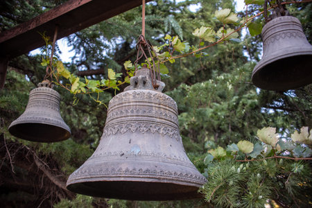 Three antique bells hanging from a wooden beam with greenery.