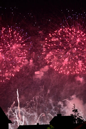 Vibrant fireworks display in the night sky, featuring pink and purple bursts with smoke and...