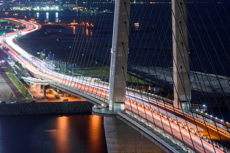 Aerial view of a bridge at night with light trails from vehicles, city lights in the background, calm water beneath, in Osaka, Japan on 30 September 2017の写真素材