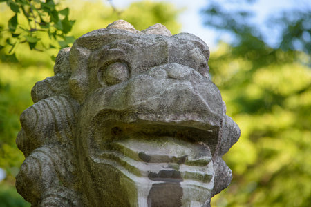 Close-up of a stone lion statue with greenery in the background.の写真素材