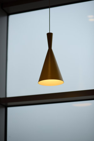 Minimalist cone-shaped pendant light against a window.の写真素材