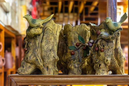 Decorative ceramic sculpture of two birds perched on textured tree-stump logs with berries, displayed on a wooden shelf in a warm, rustic indoor shop setting.の写真素材
