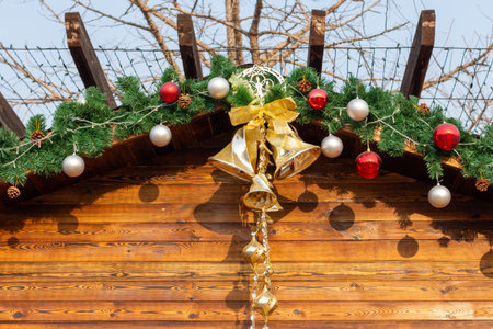 Christmas garland on wooden cabin roof with red and silver baubles, pinecones, and gold bells with ribbon, outdoors Christmas marketの写真素材
