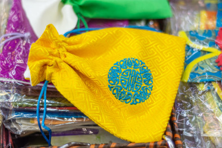 Yellow drawstring pouch with blue circular embroidery on patterned fabric, among colorful packaged textiles, close-up craft market background.の写真素材