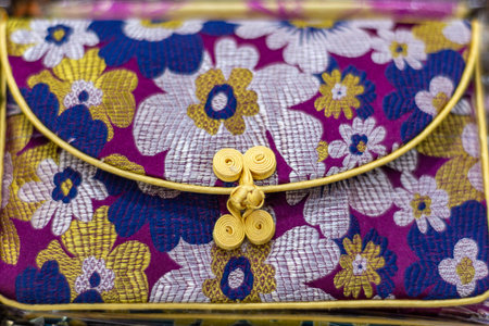 Close-up of a colorful floral brocade fabric clutch purse with gold trim and decorative clasp, showing intricate woven texture and vibrant pattern.の写真素材