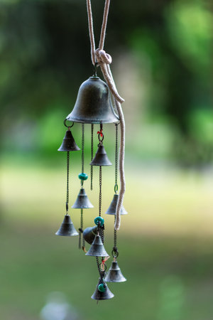 Hanging metal wind chime with multiple small bells on chains, suspended by rope outdoors with soft...
