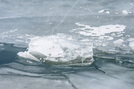 Chunk of ice or frozen slush floating on cracked winter lake surface, cold blue tones, natural...